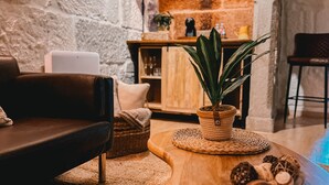 Ein gemütliches Wohnzimmer mit einem Ledersofa, einem Couchtisch aus Holz mit Dekoration, einer Topfpflanze und einer Steinwand.