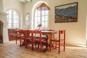 Un coin repas avec une table et des chaises en bois, de grandes fenêtres et un tableau au mur.