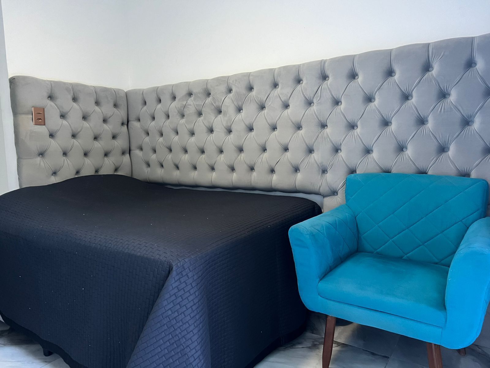 Une chambre avec un grand lit, un fauteuil bleu et une tête de lit grise à motifs.
