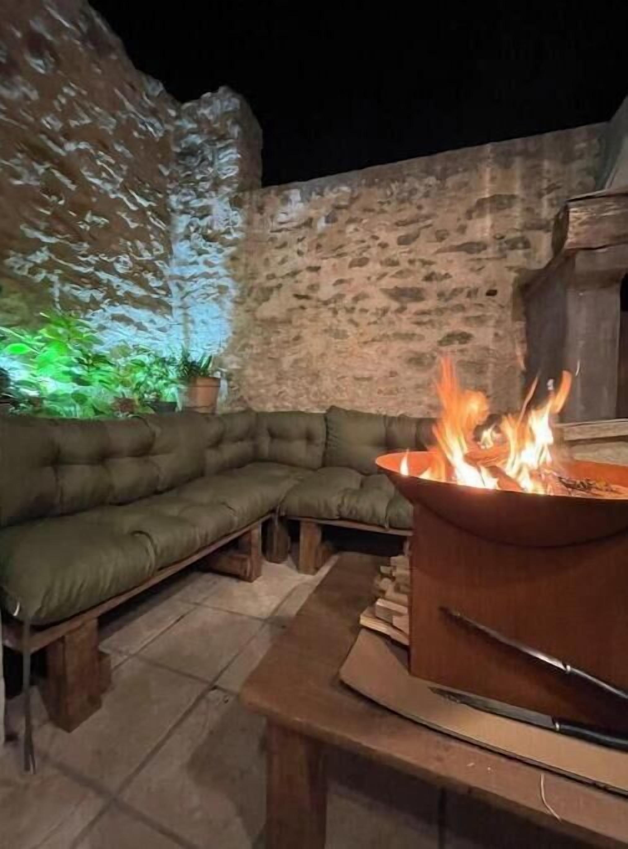 An outdoor seating area with a fire pit, stone wall, and green plants.