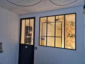 Ein Zimmer mit einer schwarzen Tür, einem Fenster mit Blick auf ein Badezimmer und einer Pflanze an der Wand.