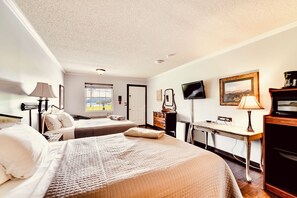 A hotel room with two beds, a desk, a television, and a view of the outdoors.