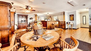 A spacious dining area with a wooden table, chairs, ceiling fans, and a kitchen in the background.