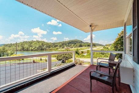 A covered balcony with a view of a lake and hills, furnished with two chairs and a table.. Deerfield Inn