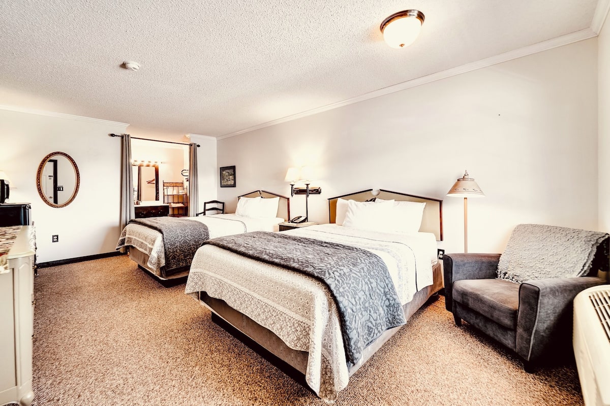 A hotel room with two beds, a chair, a desk, and a mirror.