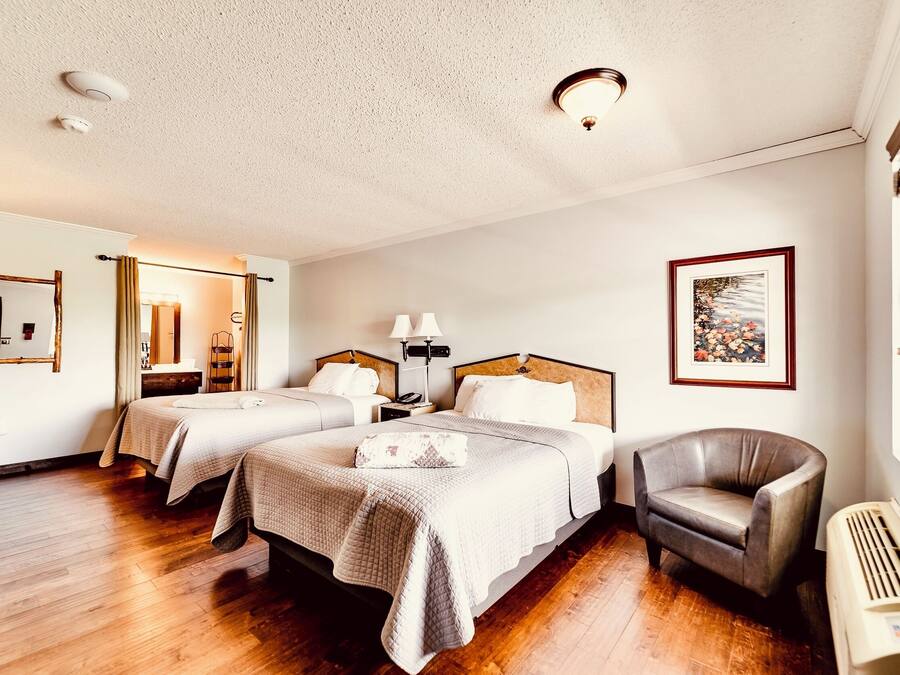 A hotel room with two beds, a chair, a desk, a mirror, a picture on the wall, and a window.