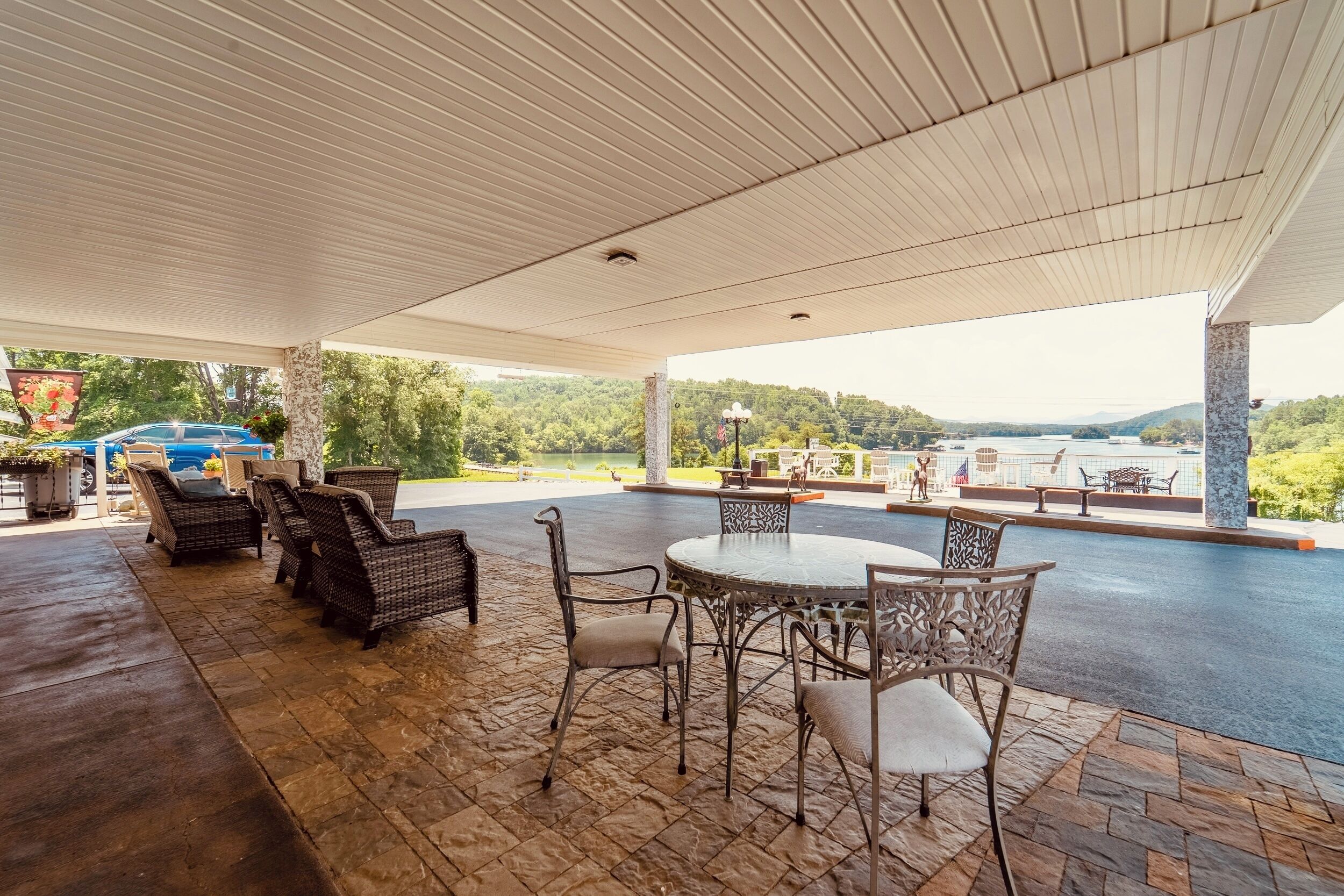 Une terrasse extérieure aménagée avec des meubles en osier, une table ronde et une vue sur un lac et des montagnes.