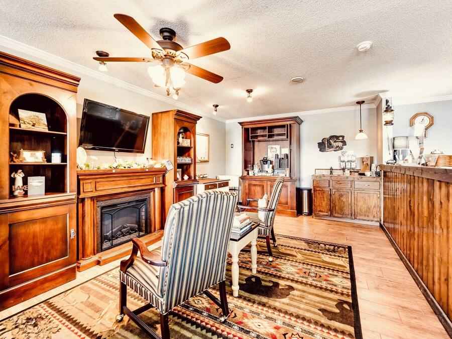 A living room with a fireplace, television, wooden cabinets, striped chairs, and a ceiling fan.