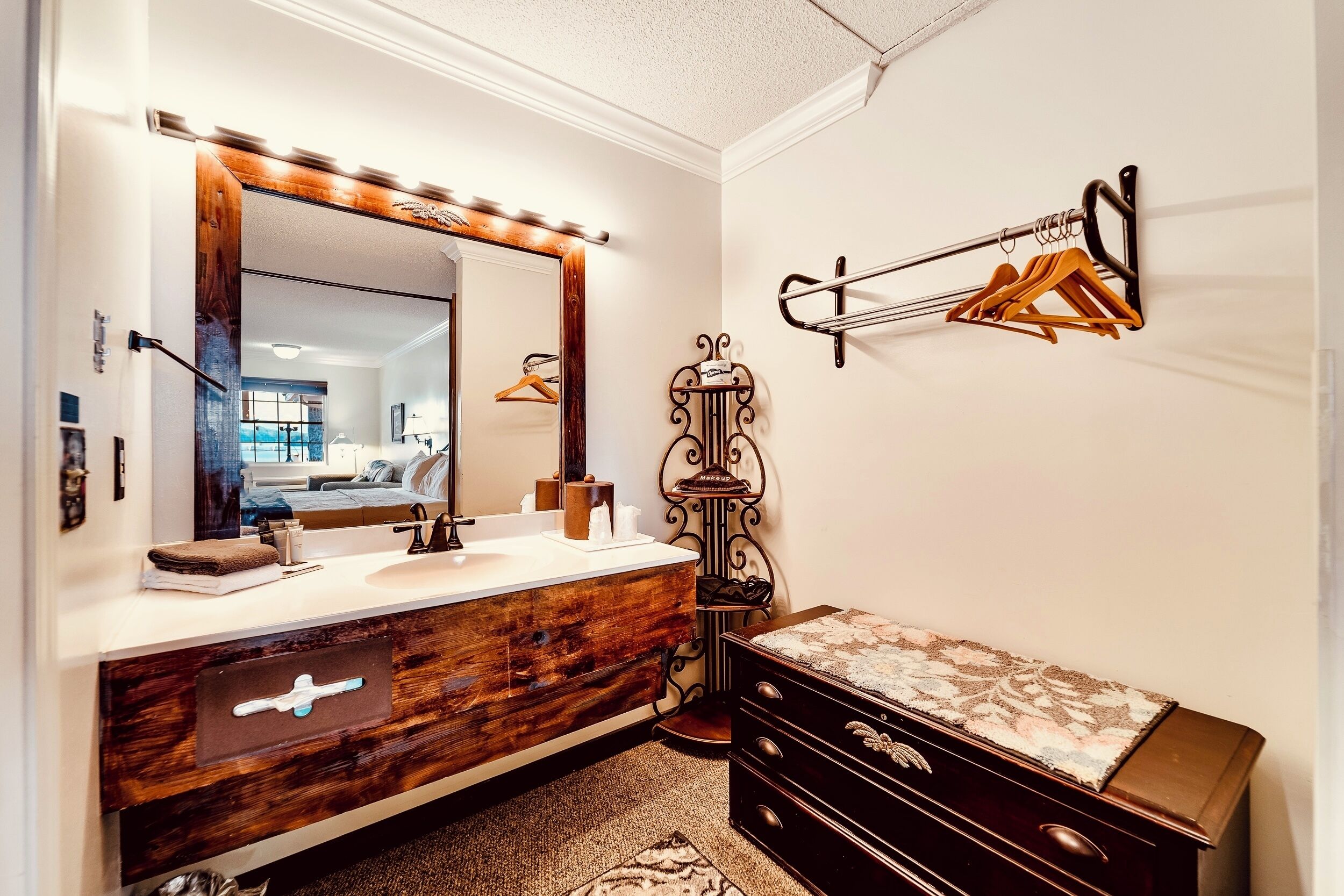 A bathroom with a wooden vanity, a large mirror with lights, a towel rack, and a small dresser.