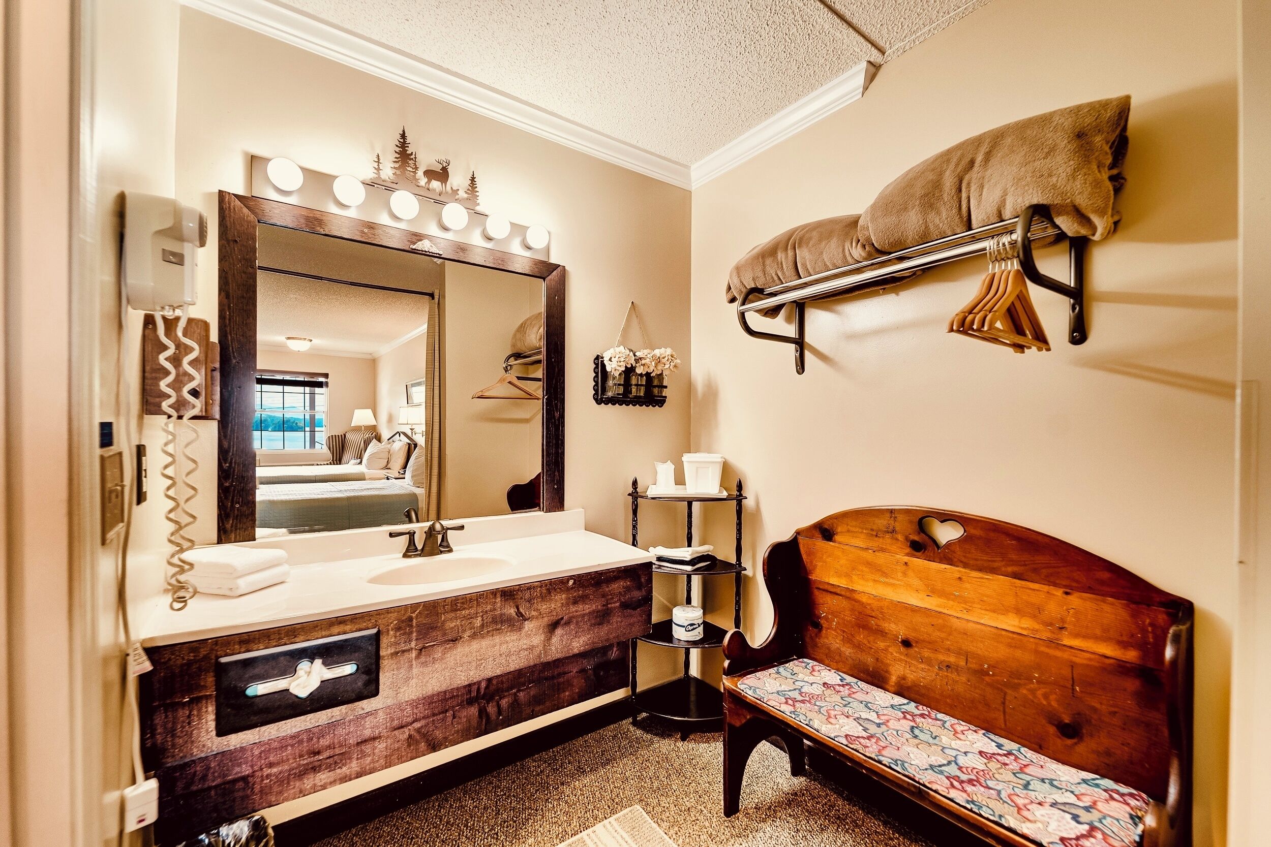 Een badkamer met een houten wastafelmeubel, een grote spiegel, een handdoekrek, een bankje en een plank met toiletartikelen.