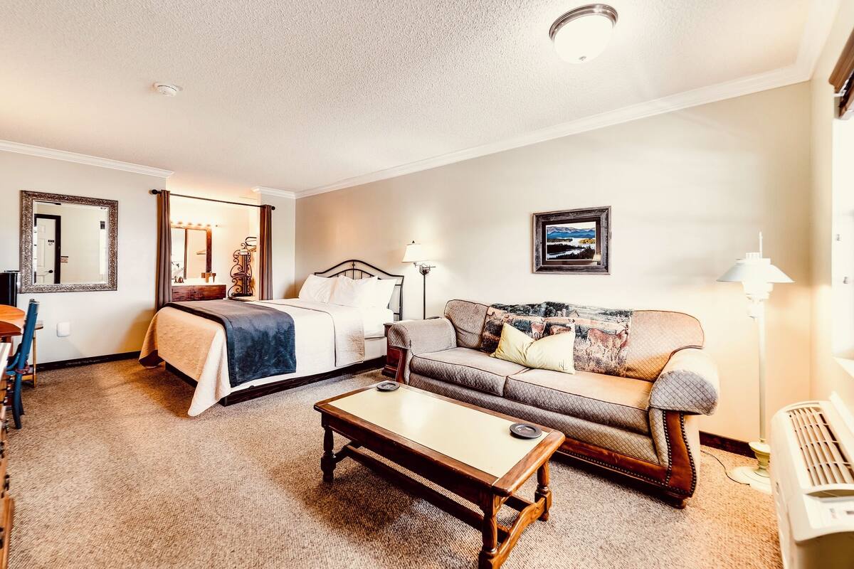 A hotel room with a bed, a sofa, a coffee table, a desk, and a lamp.