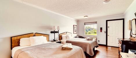 A hotel room with two beds, a desk, a chair, a lamp, and a door.