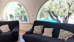 A modern living room with two dark sofas, a wooden coffee table, and large arched windows offering a view of trees and a building. - Haven of peace in a villa with pool (Antibes)