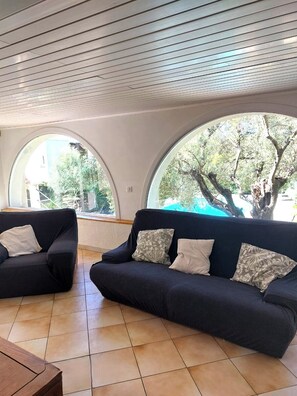 A modern living room with two dark sofas, a wooden coffee table, and large arched windows offering a view of trees and a building. - Haven of peace in a villa with pool (Antibes)