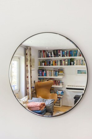 A room with a round mirror reflecting a bed, a bookshelf, and a piano. - GuestReady - Charming London Flat with Balcony (London)