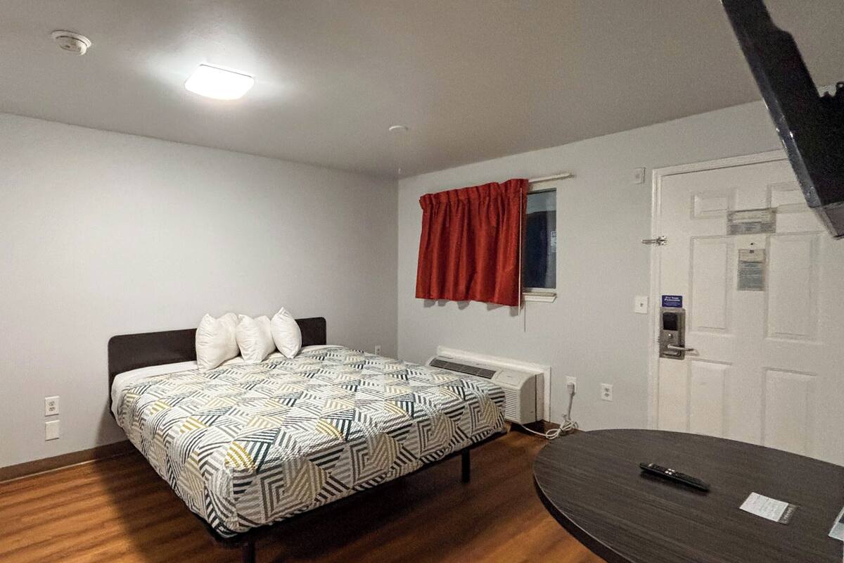 Un dormitorio con cama, escritorio, ventana con cortinas, radiador y puerta.