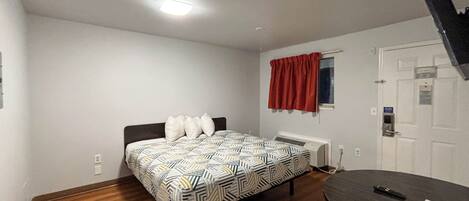 A bedroom with a bed, a desk, a window with curtains, a radiator, and a door.