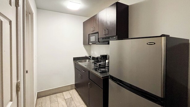 A compact kitchen with a refrigerator, microwave, and a coffee maker on the counter. - Studio 6 Greenville, SC (Greenville)