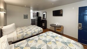 A hotel room with two beds, a small table with chairs, a TV, and a blue door. - Studio 6 Greenville, SC (Greenville)