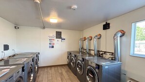 A laundry room with multiple washing machines and dryers, a ceiling light, and a window with a view of greenery outside. - Studio 6 Greenville, SC (Greenville)