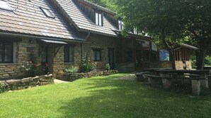 Un edificio de piedra con techo inclinado, tragaluces y un patio con césped y una mesa de picnic.