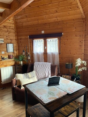 L’intérieur d’un chalet accueillant, avec un plafond en bois, une table à manger sur laquelle se trouve un ordinateur portable, un canapé et une fenêtre avec des rideaux.