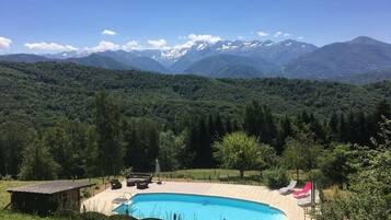 Ein Schwimmbecken mit Liegestühlen, einer Holzkonstruktion und einer Bergkulisse.