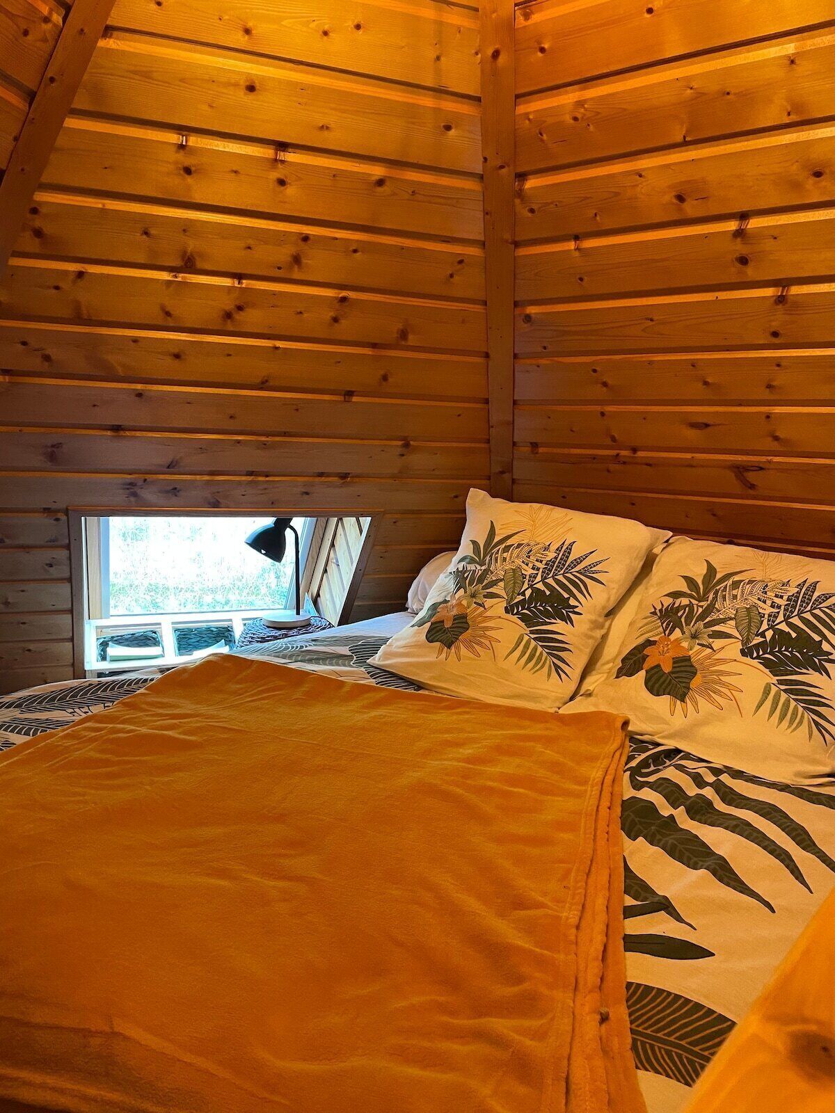 Une chambre dans une cabane en bois, avec un lit, des oreillers et une fenêtre.