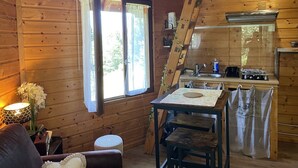 Un interior de cabaña acogedor, con comedor, cocina y un ventanal con cortinas.