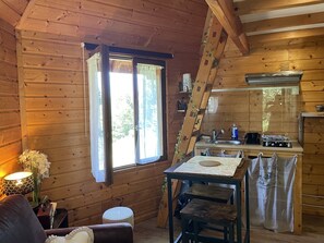 Un interior de cabaña acogedor, con comedor, cocina y un ventanal con cortinas.