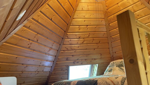 A wooden cabin room with a sloped ceiling, a bed with patterned bedding, and a window providing natural light.