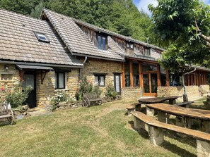Una casa de piedra con techo inclinado, bancos de madera y un pequeño jardín.