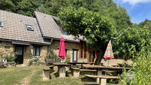 A stone building with a sloped roof, outdoor seating, and a tree in the foreground.