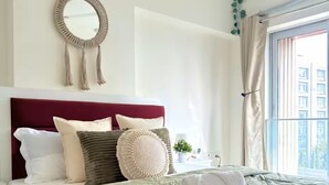 Una cama bien hecha con colcha verde, cabecera y un espejo decorativo encima.