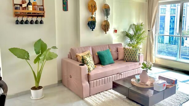 Un salón con sofá, mesa de centro, plantas en macetas, adornos en la pared y una ventana con vistas.
