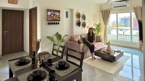 Una sala de estar moderna con comedor, sofá, ventiladores de techo y un amplio ventanal con vista a la ciudad.