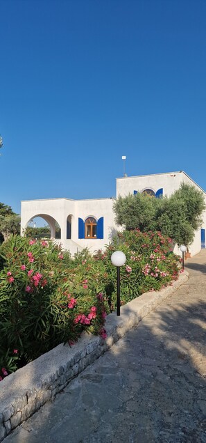 A building with white walls and blue accents, surrounded by greenery and flowers. - Beautiful vacation villa in the heart of Puglia Castellana Grotte (Puglia)