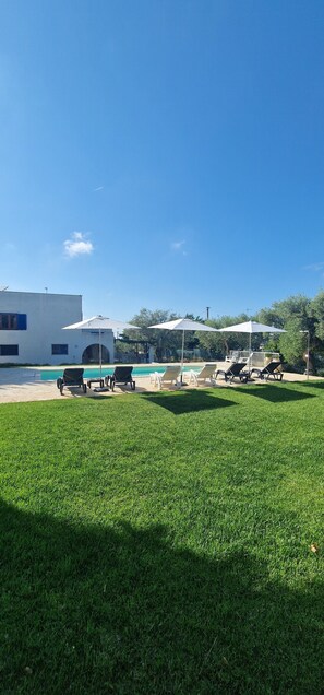 A pool area with lounge chairs, umbrellas, and a building in the background. - Beautiful vacation villa in the heart of Puglia Castellana Grotte (Puglia)