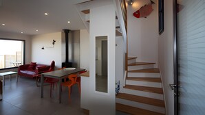 Um interior moderno com escada, área de jantar com mesa e cadeiras, sofá vermelho e decoração de peixe na parede.