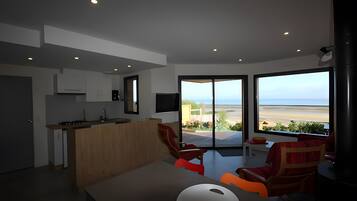 Un intérieur moderne comprenant une cuisine, un coin repas et une grande porte-fenêtre coulissante donnant sur un balcon avec vue sur la plage.