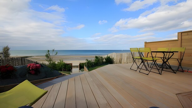 Um deck de madeira com mobiliário para área externa, com vista para uma praia.