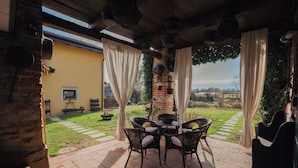 An outdoor patio with wicker chairs and a table, a brick wall, and a view of the countryside. - The Willow Bed & Breakfast - Room Sage (Veruno)