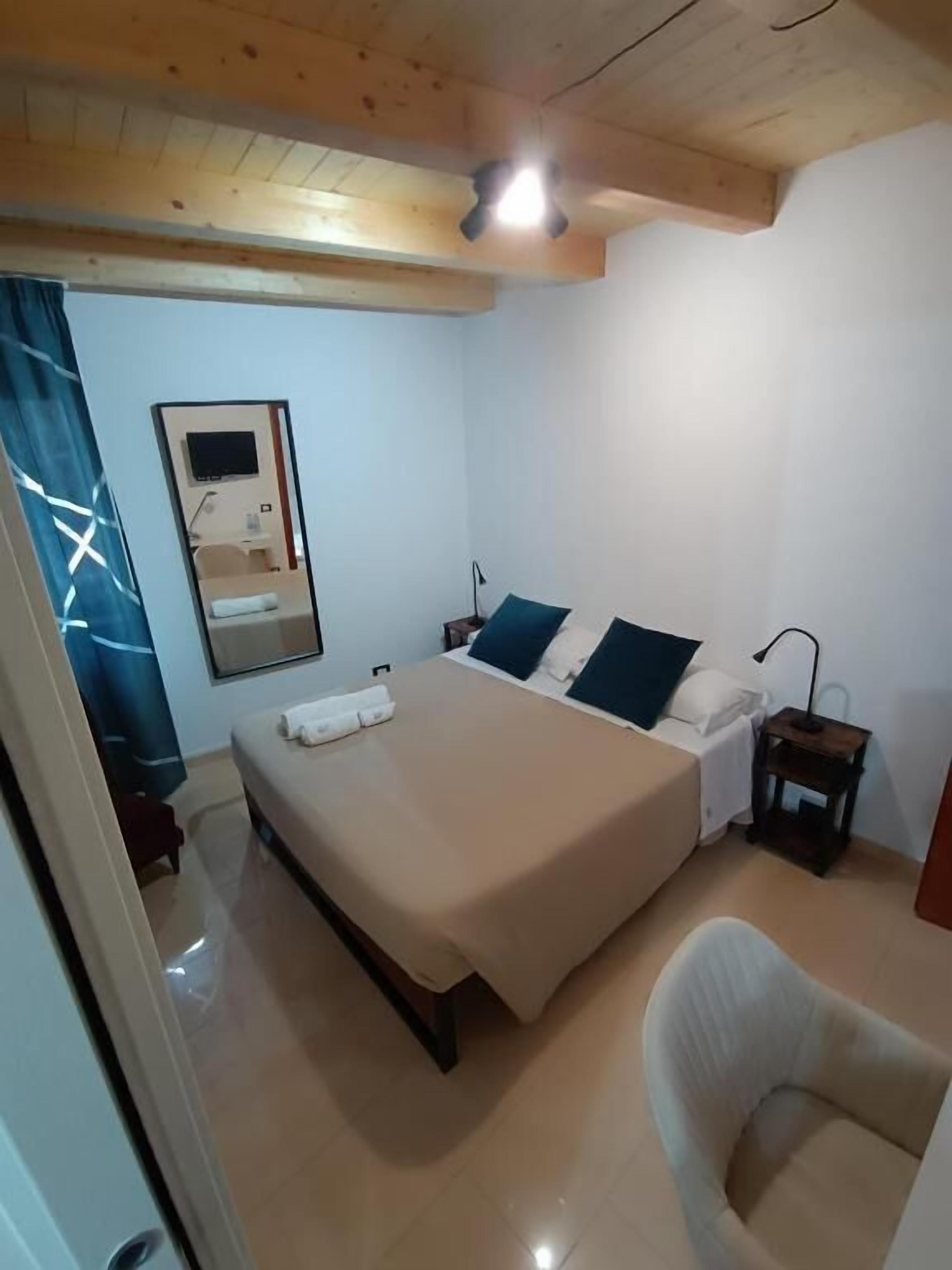 A bedroom with a bed, a bedside table, a chair, a mirror, and a TV.