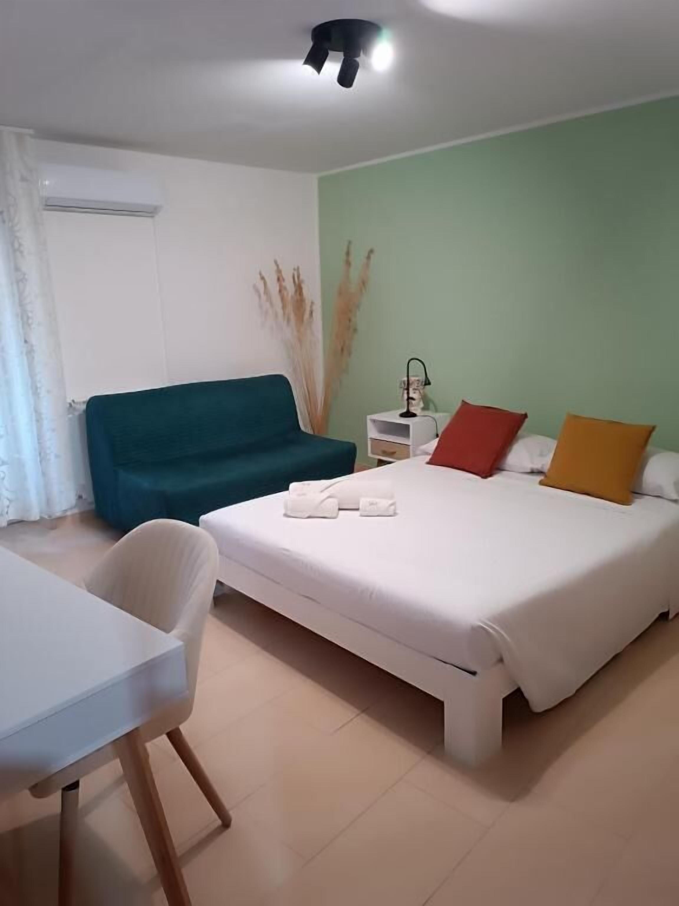 Una habitación de hotel con cama, escritorio, silla, mesita de noche y ventilador de techo.