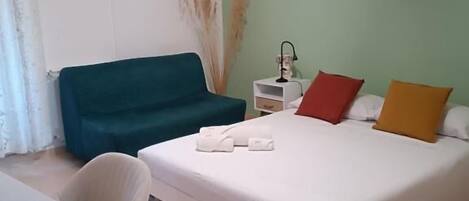 Una habitación de hotel con cama, escritorio, silla, mesita de noche y ventilador de techo.