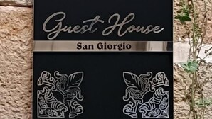 A black sign with white decorative patterns and text reading 'Guest House San Giorgio.' - Guest House San Giorgio (Caltagirone)