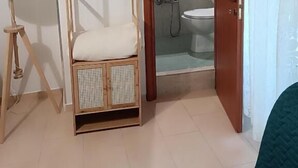 A room with a hanging chair, a bedside table, a lamp, and a view into a bathroom with a toilet and sink. - Guest House San Giorgio (Caltagirone)
