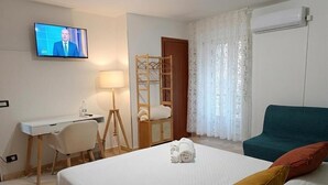 A hotel room with a bed, a desk, a chair, a television, and a window with curtains. - Guest House San Giorgio (Caltagirone)
