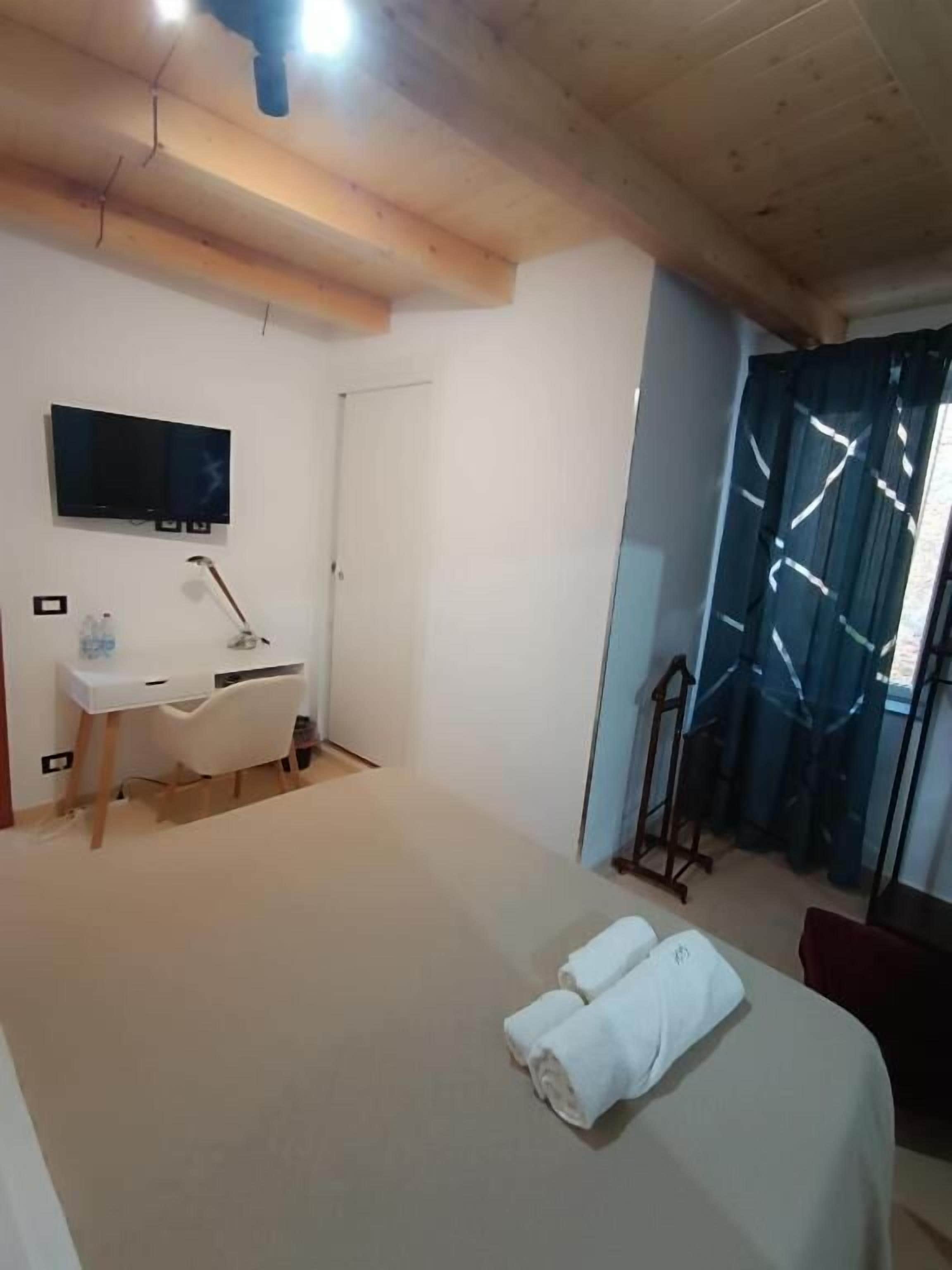Ein Schlafzimmer mit einem Bett, einem Schreibtisch, einem Stuhl, einem Fernseher und einem Fenster mit Vorhängen.