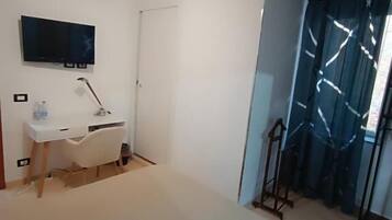Ein Schlafzimmer mit einem Bett, einem Schreibtisch, einem Stuhl, einem Fernseher und einem Fenster mit Vorhängen.